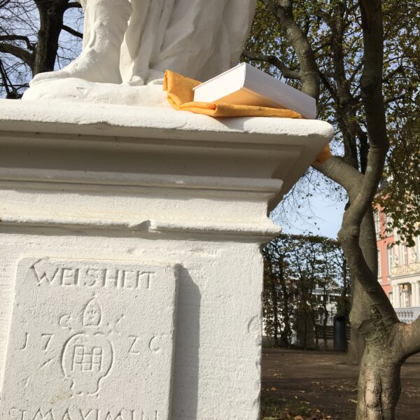 Bild der Weisheits-Statue beim Kurfürstlichen Palais Trier mit einem Band der "Zehn keinen Bücherlein".