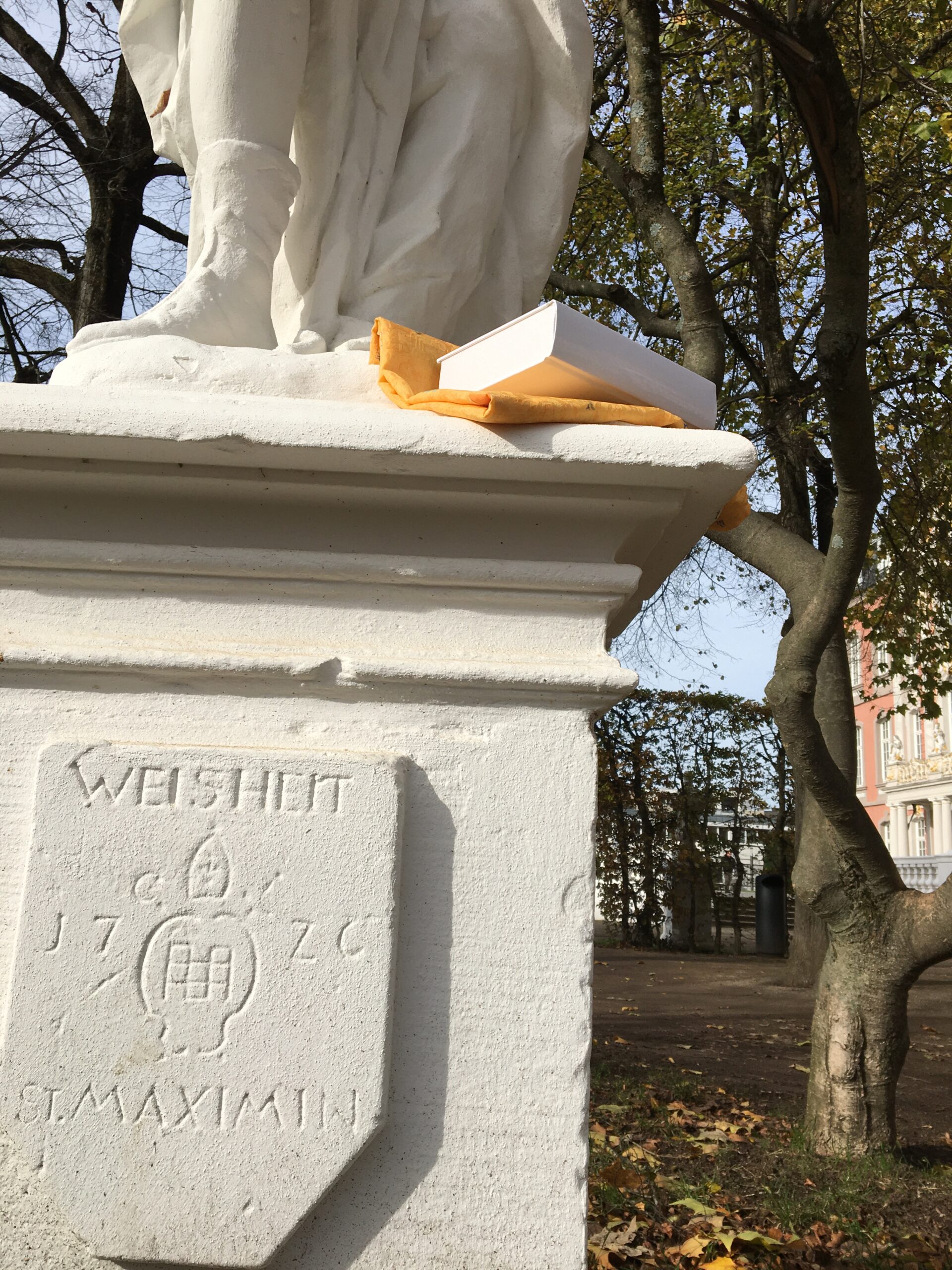 Bild der Weisheits-Statue beim Kurfürstlichen Palais Trier mit einem Band der "Zehn keinen Bücherlein".